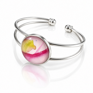 A silver-toned double-band cuff bracelet featuring a round bezel-set cabochon with a pink and white marbled pattern and a yellow-green accent, shown on a reflective white surface.