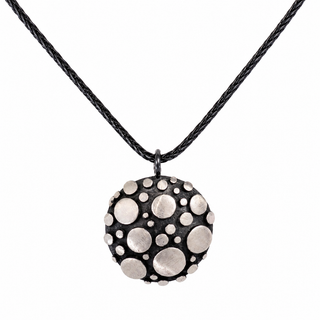 A black braided cord necklace with a round textured pendant featuring raised silver-tone metallic circles on a black background, shown against a plain white background.