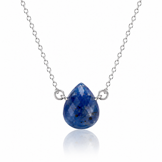 A silver chain necklace featuring a faceted teardrop-shaped blue gemstone pendant with silver filigree accents, displayed on a clean white background with a soft reflection below.