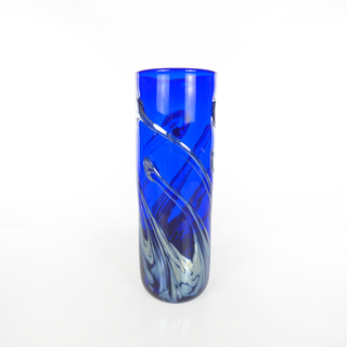 A tall, cylindrical cobalt blue glass vase with abstract silver and white swirl patterns, photographed on a seamless white background.